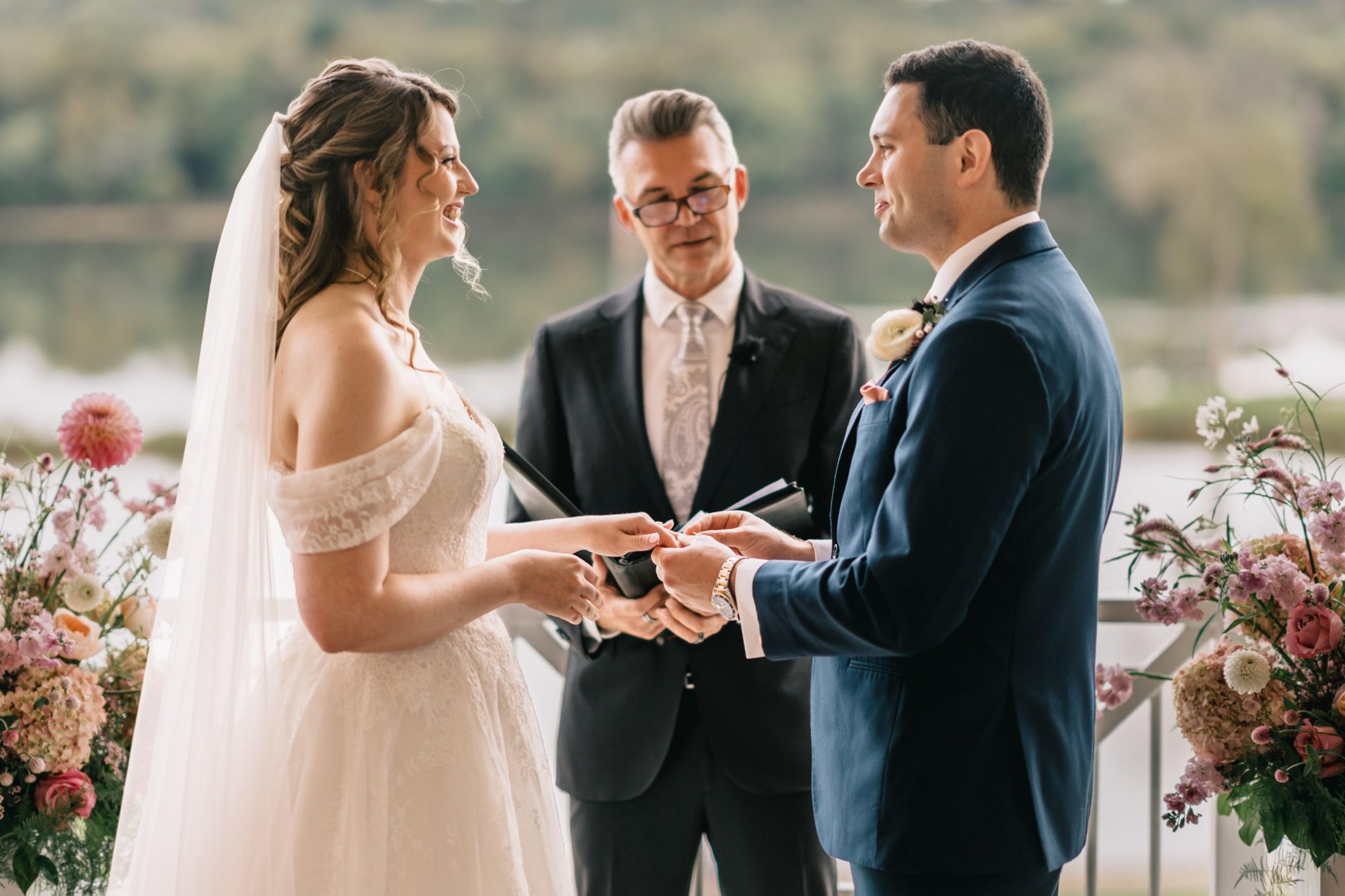 Wedding officiant Loren Hudziak guiding a bride and groom through a ring exchange at an outdoor ceremony